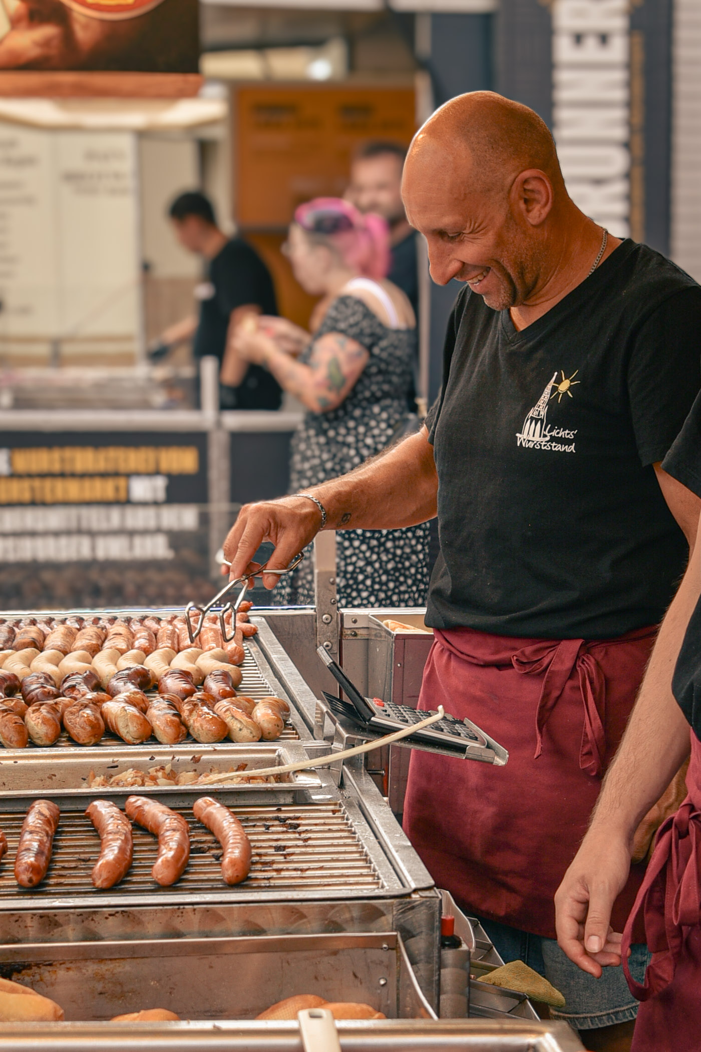 Mitarbeiter am Grill mit Zange und Bratwürsten