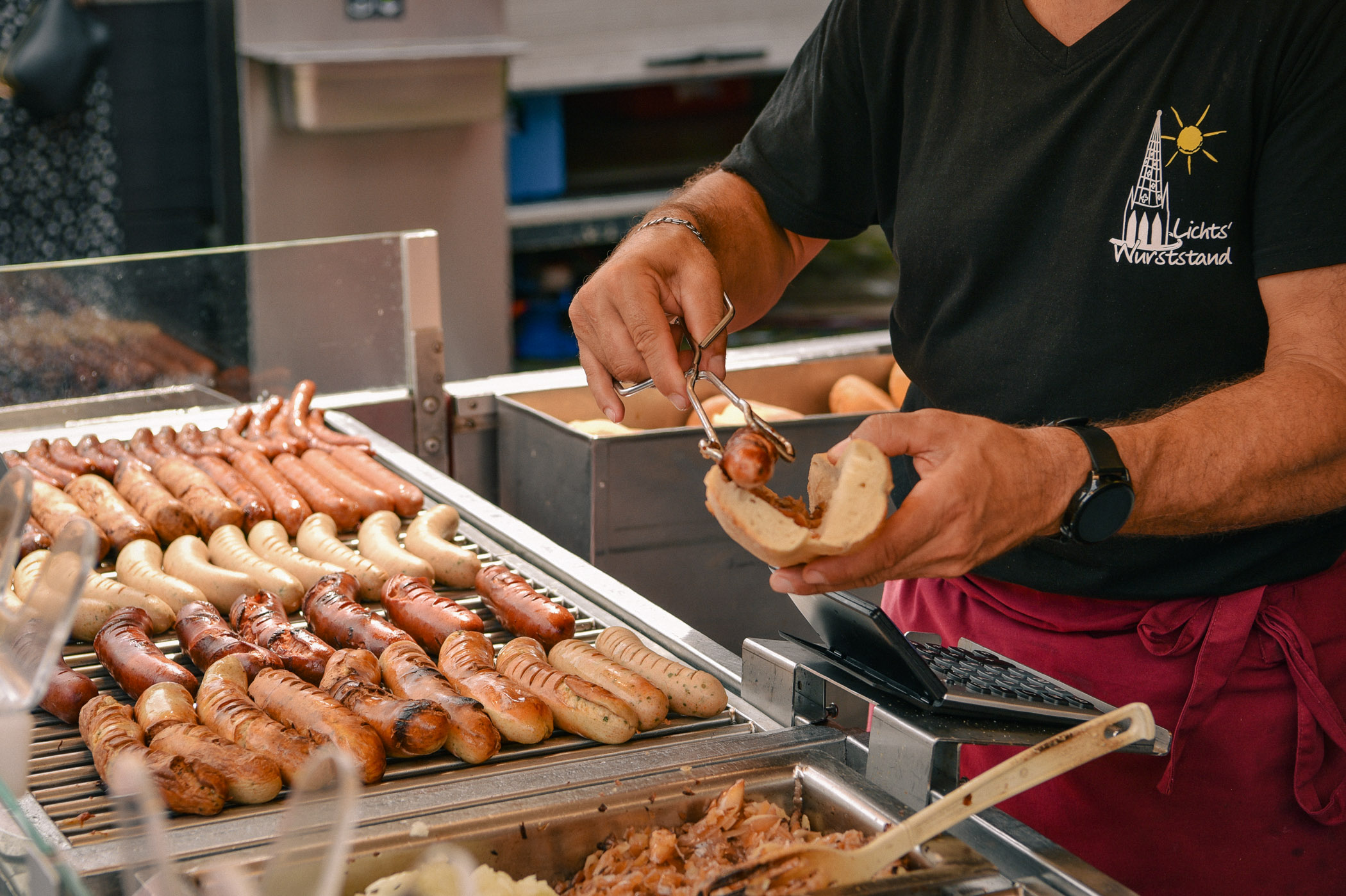Wurst wird mit Zange ins Brötchen gelegt