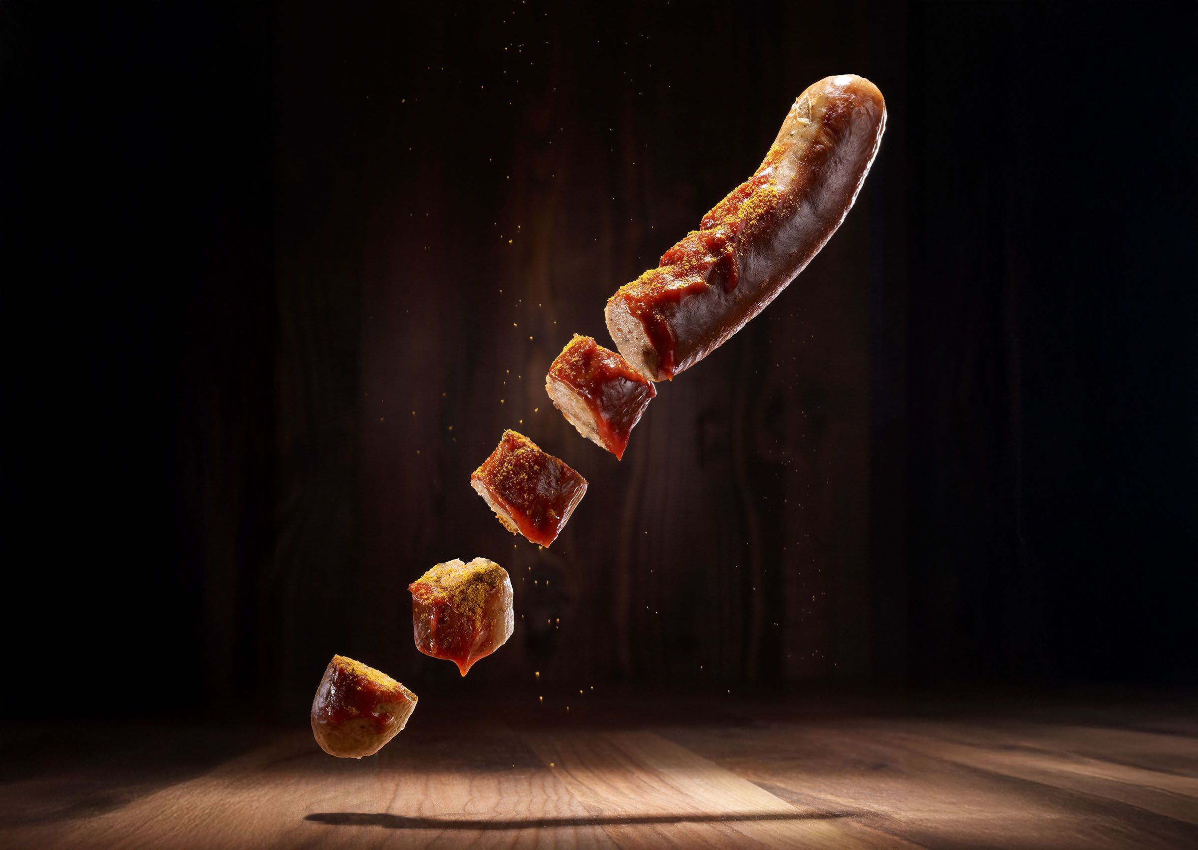 Schwebende, geschnittene Bratwurst vor dunklem Hintergrund.